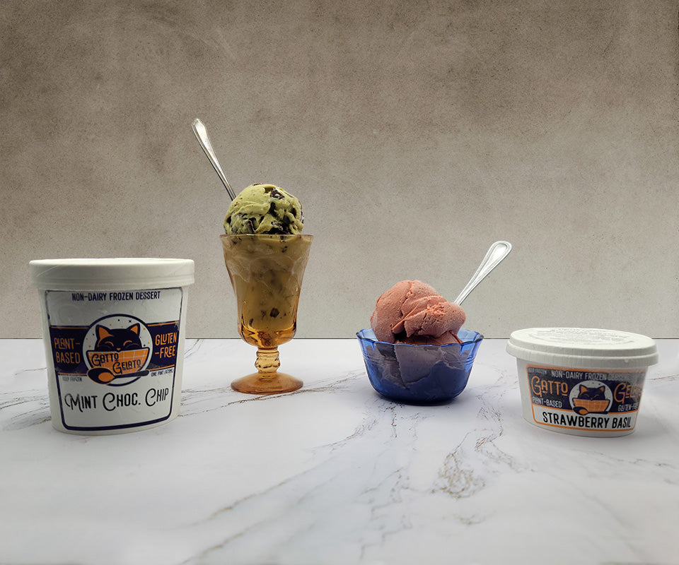 Marble countertop with a pint of mint chocolate chip non-dairy gelato, a packaged 4 ounce single-serving of strawberry non-dairy gelato, and a scoop of each in glass ice cream dishes.