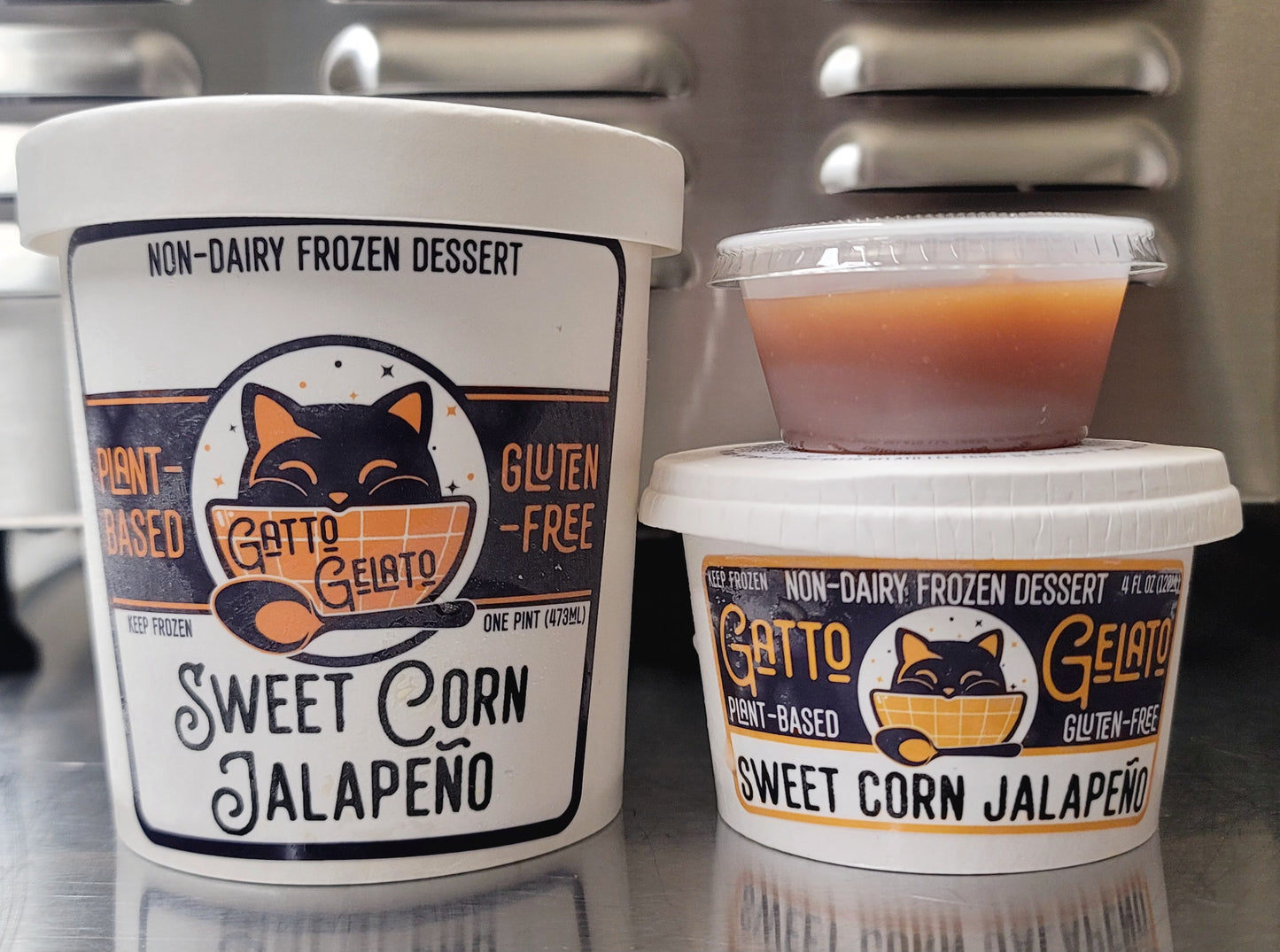 Two containers of Gatto Gelato Sweet Corn Jalapeno non-dairy frozen dessert on a reflective surface.